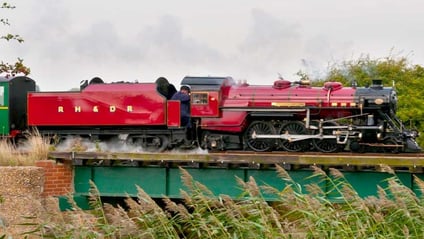 A red steam locomotive on the Romney, Hythe and Dymchurch Railway crossing a bridge